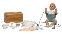 1203.  Juanín bebé con taca-taca.Muñeco de cartón piedra con ojos durmientes. Acompaña baulito de madera con ropa y menaje.España, h. 1940.