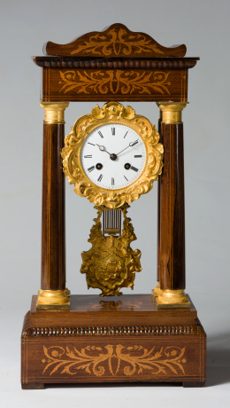 1135.  Reloj de sobremesa “de pórtico” Napoleón III, en madera de palosanto con marquetería de limoncillo y aplicaciones de bronce dorado.Trabajo francés, segunda mitad S. XIX