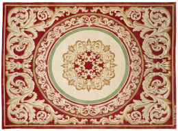 1056.  Alfombra en lana de estilo Carlos IV, de fondo granate hojas, formando roleos y medallón central, frimada. Miguel Stuyck..