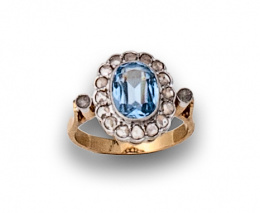 39.  Sortija rosetón años 40 con piedra  azul y orla de diamantes en oro de 18K con frente de platino.