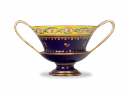 1291.  Taza de dos asas de porcelana esmaltada en azul de cobalto y dorada, con cenefa de flores con cintas.Sévres, h. 1795