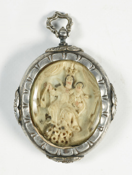 446.  Medallón devocional de marfil tallado y policromado; en el anverso representa la trinidad Isomorfa y  en el reverso la Virgen del Carmen,  marco de plata, con decoración repujada de querubines.Trabajo mexicano, S.XVIII..