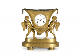 486.  Reloj de sobremesa Imperio en bronce dorado, en el que dos ángeles sujetan una cesta que hace las veces de caja del reloj. Francia, primer tercio del S. XIX