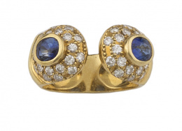144.  Sortija con dos zafiros ovales orlados de brillantes, en montura de frente abierto de oro amarillo de 18K.
