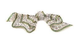 808.  Broche lazo de brillantes y esmeraldas calibradas, sobre trabajo que simula puntilla con dibujo de hojitas plegada.