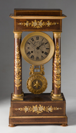 1171.  Reloj de sobremesa de “pórtico” Napoleón III en madera de palosanto con marquetería de maderas finas y aplicaciones de bronce dorado.Trabajo francés, segunda mitad S. XIX.