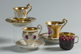 875.  Conjunto de cuatro tazas; tres con plato, una de Viena, dos en porcelana de París, esmaltadas, doradas a fuego y pintadas, una de época Carlos X, h. 1820 - 1830, otra dorada en rosa y dorada, con un soporte de plata, S. XIX.