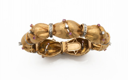 198.  Brazalete con diseño en forma de banda arqueada de oro mate, anudada por arcos de diamantes y decorada en los centros de cada pieza por parejas de rubíes y brillantes centrales