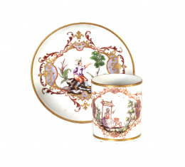 1085.  Taza y plato de porcelana esmaltada con dos campesinos entre rocalla.Alemania, h. 1800..