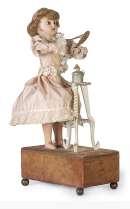 1159.  Renuou. Autómata. Niña con tenacillas para rizarse el pelo.Cabeza de Biscuit de Jumeau, boca cerrada, ojos de pasta vítrea, vestido de raso en seda, madera pintada, peluca rubia y caja de terciopelo marrón.Francia, ff. del S. XIX.