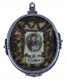 396.  Reliquia con grabado coloreado de San Nicolás e hilos metálicos a cordoncillo, en el reverso auténtica, marco de plata en su color con cordoncillo y flores aplicadas.S. XVIII.