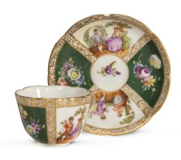 1243.  Taza con plato de porcelana esmaltada y dorada con personajes y flores. Marcas en la base en azul cobalto.Helena Wolfsohn, Dresden, finales del S. XIX.