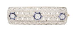 98.  Broche placa Art-Decó con decoración calada y diamantes, con tres centros de chatones de brillantes con marco de estrellas de zafiros calibrados