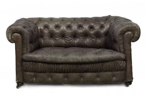 Sofá “chesterfield” con tapicería capitoné de piel marrón.