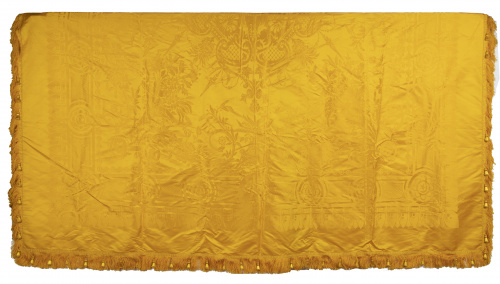 Colcha de raso amarillo rematada por flecos y pasamanería.